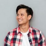 pria muda asia tersenyum berdiri di depan dinding abu abu 171337 10473